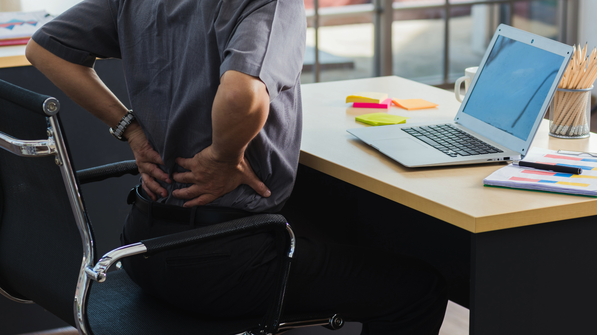 Person sitting on an office chair holding their back in pain due to poor posture.